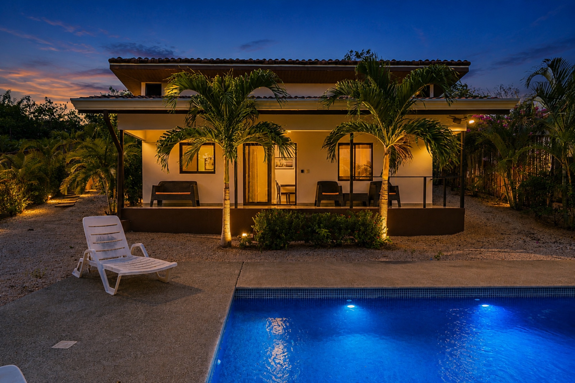 Lit villa facade with palms at dusk