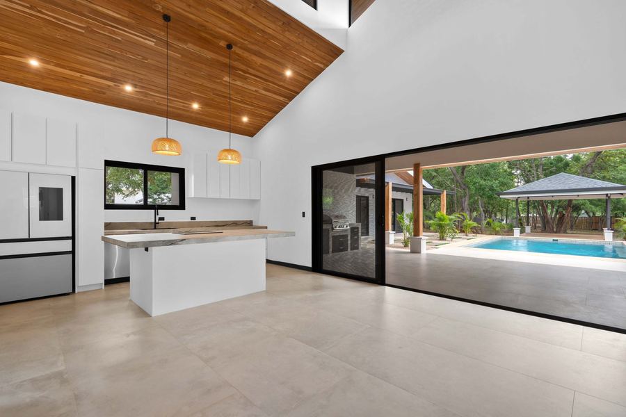 The great room — chef’s kitchen under a cathedral teak ceiling, open to the pool on both sides