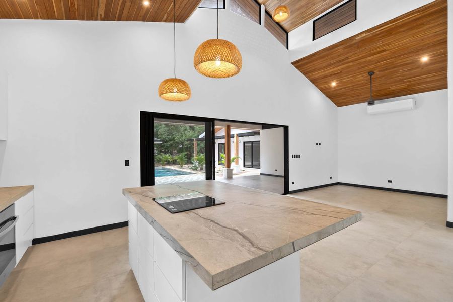 Stone-topped island with induction cooktop beneath woven pendants