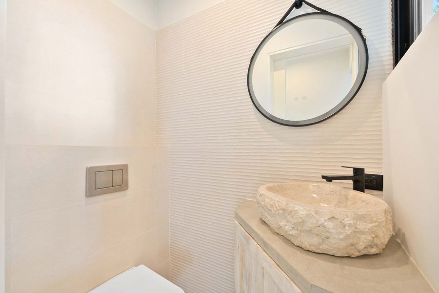 Bath detail — textured tile, round mirror, and stone basin
